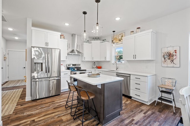 kitchen with a kitchen island, stainless steel appliances, light countertops, wall chimney range hood, and white cabinetry
