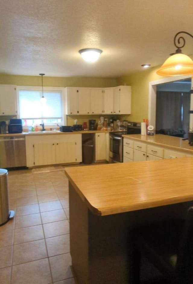 kitchen featuring a textured ceiling, light tile patterned flooring, stainless steel appliances, a sink, and decorative light fixtures