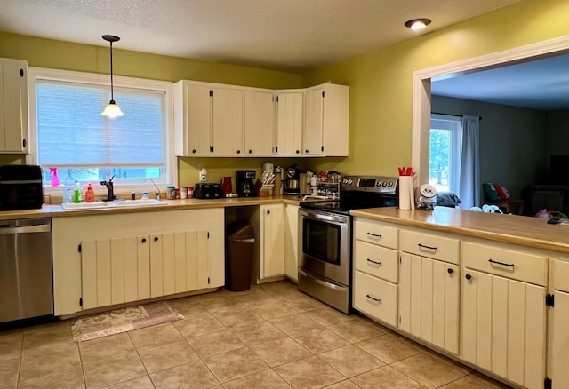 kitchen featuring appliances with stainless steel finishes, hanging light fixtures, light countertops, white cabinetry, and a sink