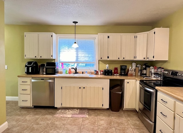 kitchen featuring white cabinets, decorative light fixtures, stainless steel appliances, light countertops, and a sink