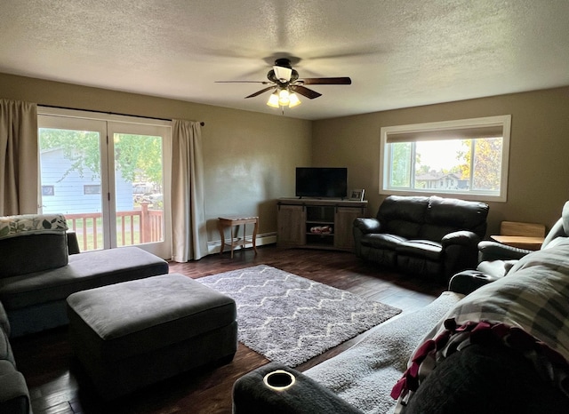 living room with a baseboard heating unit, a textured ceiling, dark wood finished floors, and a wealth of natural light