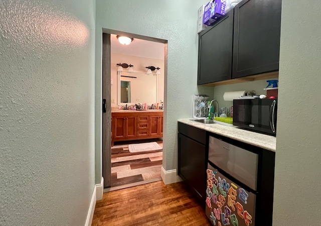 bar featuring a textured wall, a sink, wood finished floors, black microwave, and baseboards