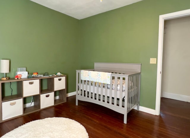 bedroom featuring a nursery area, dark wood-type flooring, and baseboards