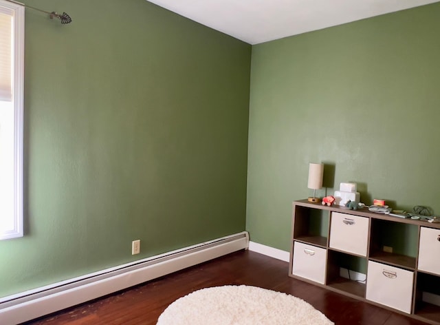 recreation room featuring a baseboard heating unit, dark wood-style floors, and baseboards