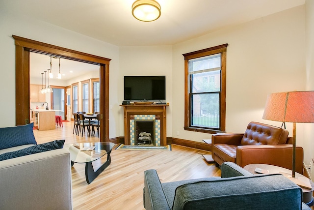 living room with a tile fireplace, baseboards, and wood finished floors