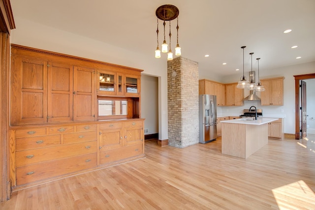 kitchen featuring pendant lighting, light countertops, stainless steel fridge, a center island with sink, and ornate columns