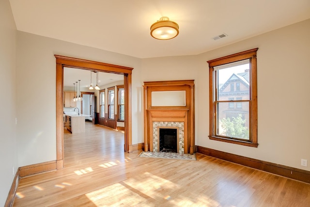 unfurnished living room with visible vents, a premium fireplace, light wood-style floors, a sink, and baseboards