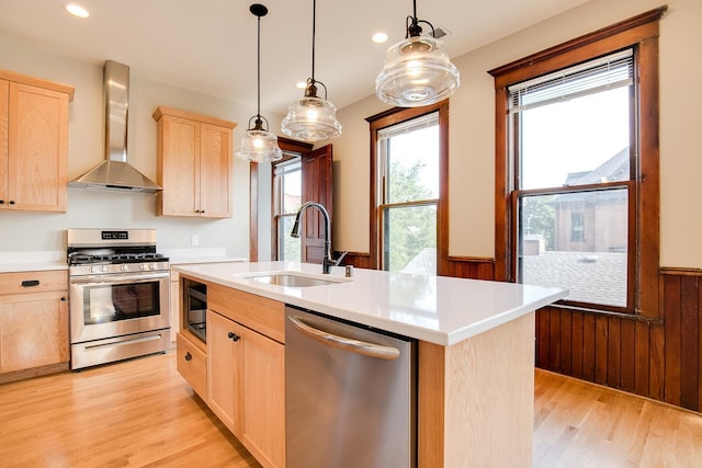 kitchen featuring an island with sink, wall chimney exhaust hood, appliances with stainless steel finishes, light countertops, and light brown cabinets