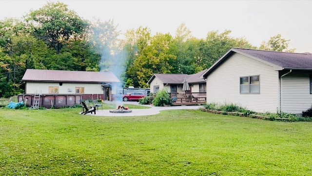 rear view of property with a deck, a fire pit, an outdoor pool, and a lawn