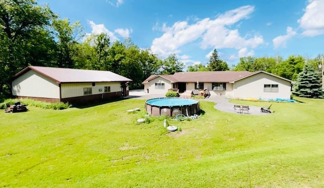 back of property with an outdoor fire pit, a lawn, and a covered pool