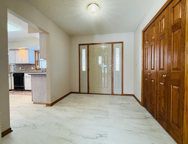 foyer entrance featuring marble finish floor, a textured ceiling, and baseboards