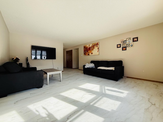 living area featuring a textured ceiling, marble finish floor, and baseboards