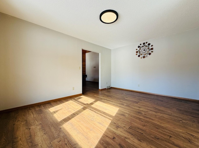 empty room featuring a textured ceiling, baseboards, and wood finished floors