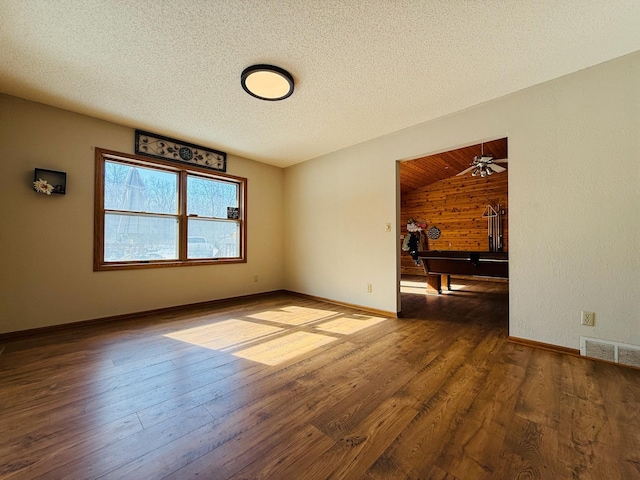 spare room featuring visible vents, a textured ceiling, baseboards, and dark wood-type flooring