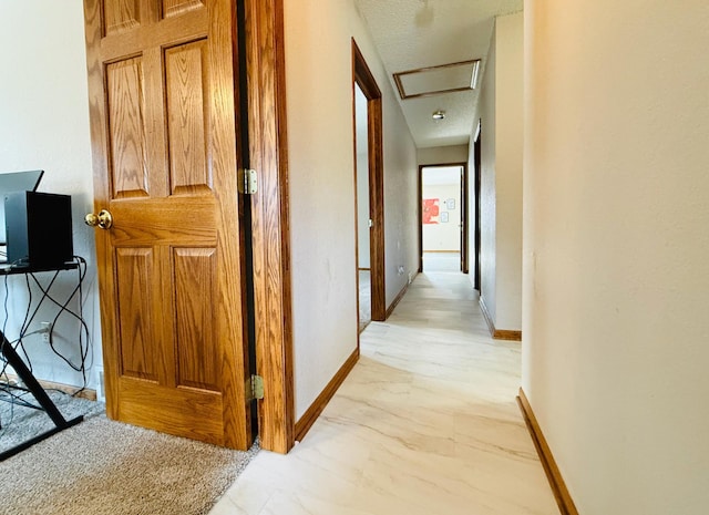 hallway featuring marble finish floor, attic access, and baseboards