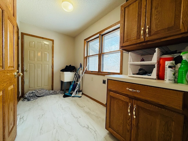 laundry area with marble finish floor, a textured ceiling, baseboards, and cabinet space