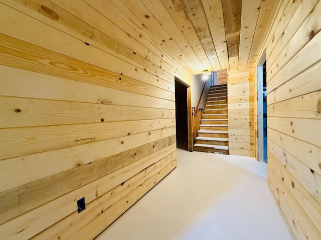 hall featuring wooden ceiling, wooden walls, and stairway