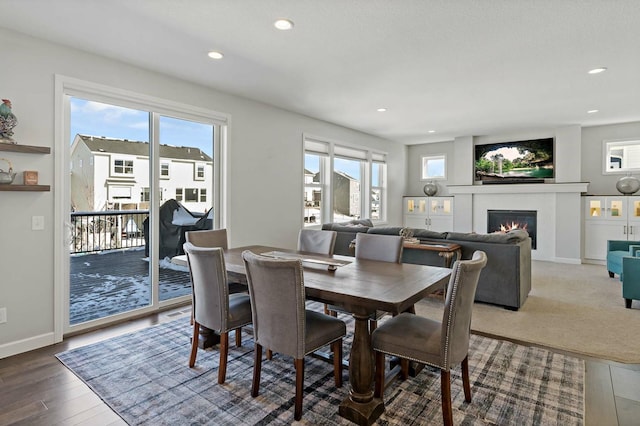 dining area featuring a glass covered fireplace, wood finished floors, baseboards, and recessed lighting