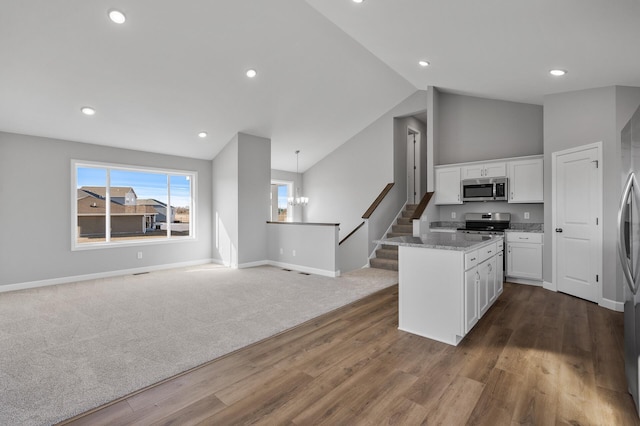 kitchen featuring lofted ceiling, light stone counters, stainless steel appliances, white cabinetry, and open floor plan