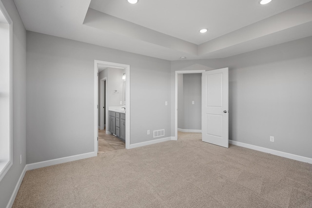 unfurnished bedroom with light colored carpet, a raised ceiling, visible vents, and baseboards