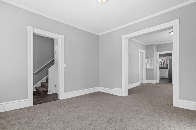 carpeted empty room with crown molding, baseboards, and stairs