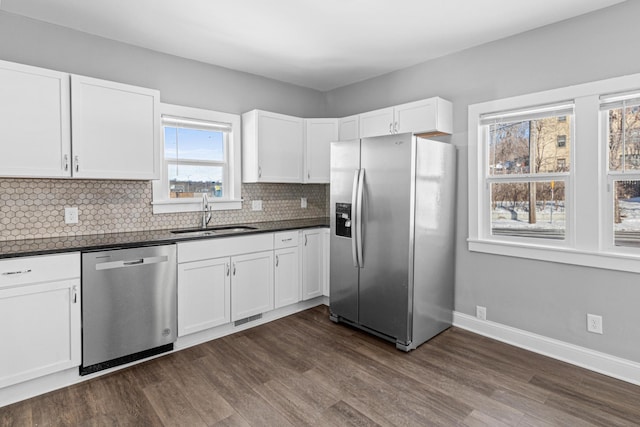 kitchen with dark countertops, backsplash, appliances with stainless steel finishes, white cabinetry, and a sink