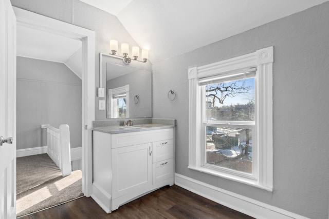 bathroom with vaulted ceiling, vanity, baseboards, and wood finished floors