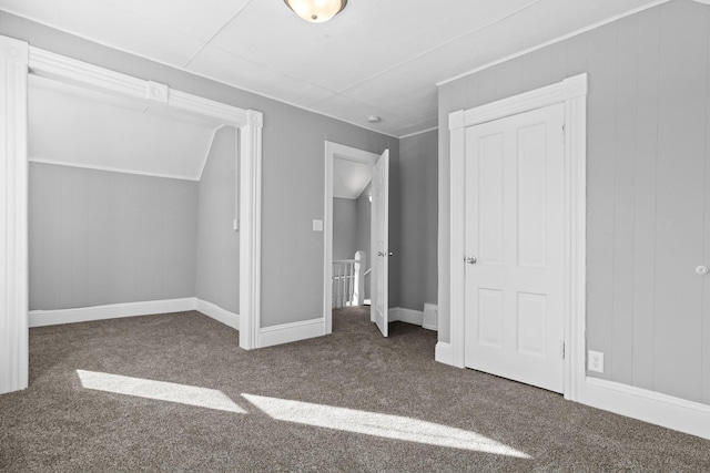 unfurnished bedroom with vaulted ceiling, dark colored carpet, and baseboards