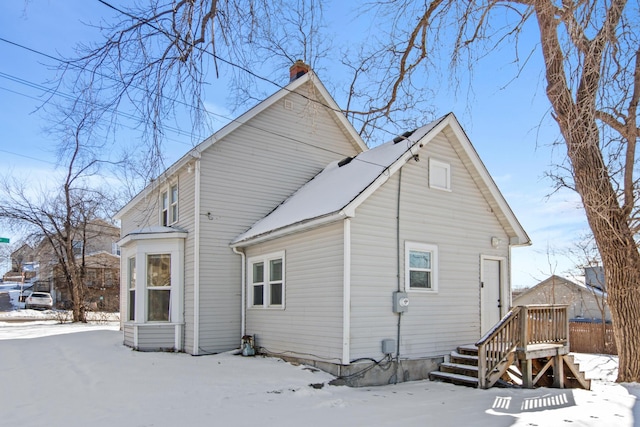 snow covered back of property featuring a chimney