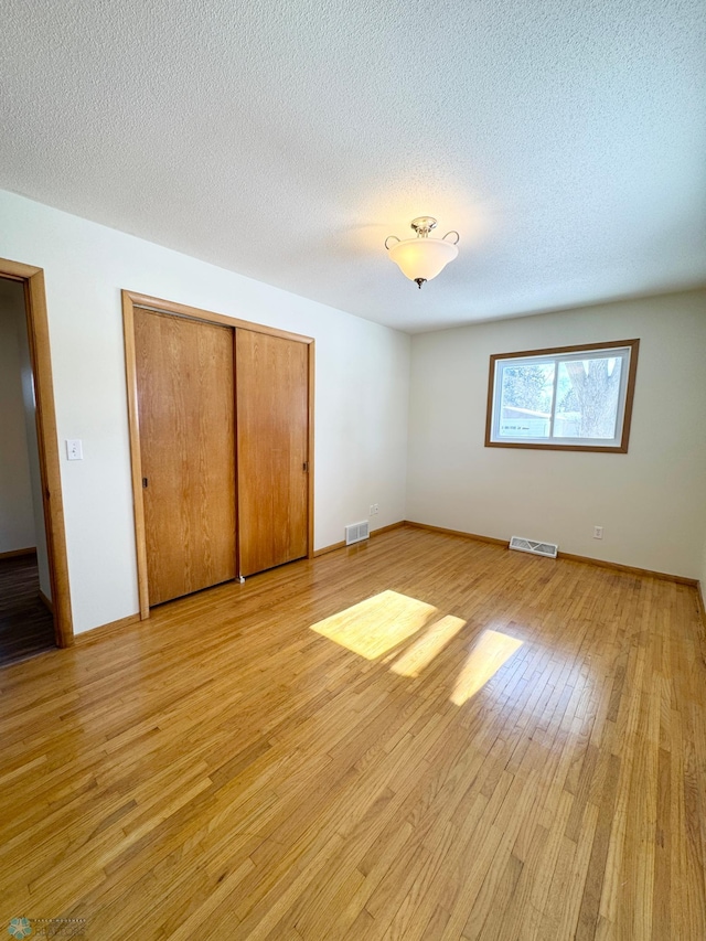 unfurnished bedroom featuring a closet, visible vents, a textured ceiling, and light wood finished floors