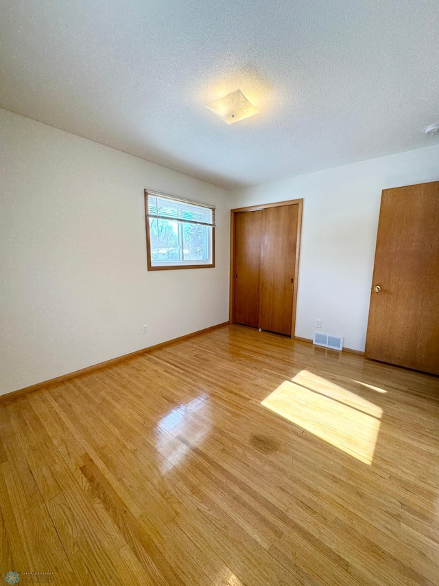 unfurnished bedroom featuring a textured ceiling, light wood-style flooring, visible vents, baseboards, and a closet