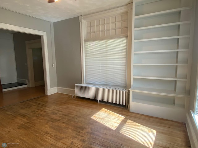 spare room featuring radiator heating unit, wood finished floors, and baseboards