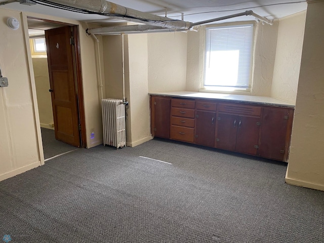 basement featuring baseboards, light colored carpet, a textured wall, and radiator heating unit