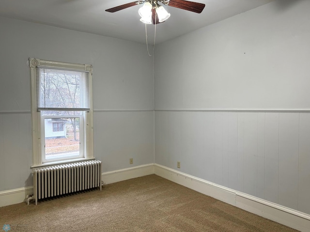 carpeted spare room featuring radiator heating unit, ceiling fan, and wainscoting