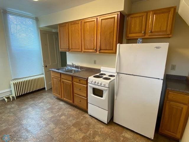 kitchen featuring white appliances, brown cabinetry, dark countertops, radiator heating unit, and a sink