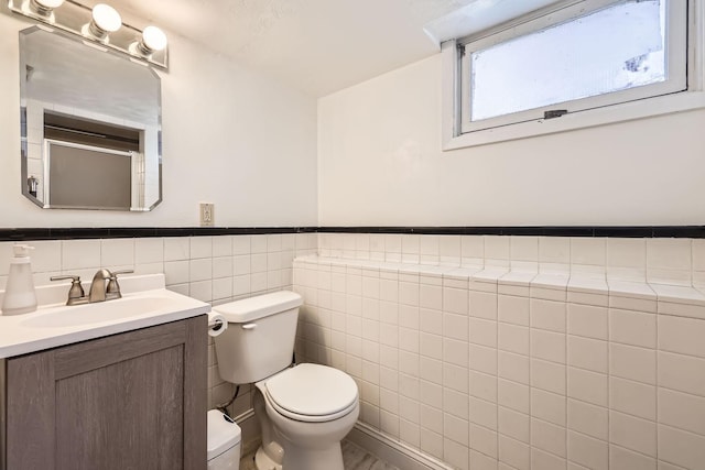 bathroom featuring wainscoting, vanity, toilet, and tile walls