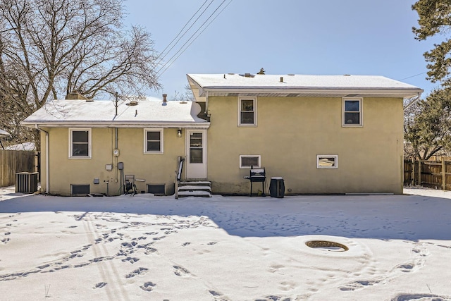 snow covered rear of property featuring entry steps, fence, a chimney, and stucco siding