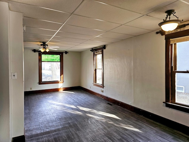 empty room with ceiling fan, a drop ceiling, baseboards, and wood finished floors