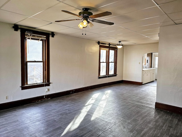 unfurnished room featuring baseboards, ceiling fan, a drop ceiling, wood finished floors, and arched walkways