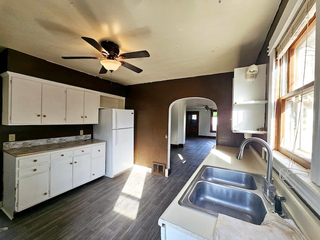 kitchen featuring a ceiling fan, arched walkways, freestanding refrigerator, a sink, and dark wood-type flooring