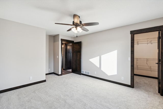 unfurnished bedroom featuring a walk in closet, light carpet, visible vents, and baseboards