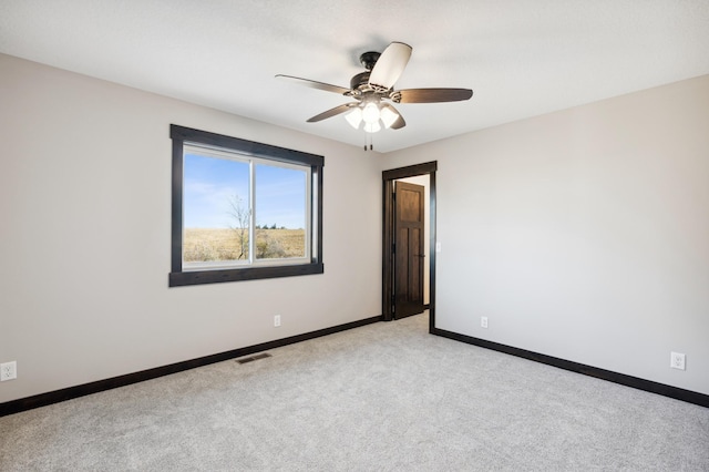 empty room with light carpet, a ceiling fan, visible vents, and baseboards