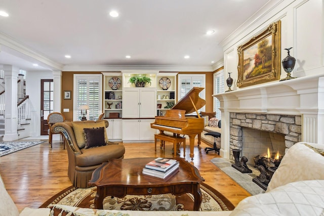 living area with light wood-style floors, ornamental molding, a stone fireplace, and stairs