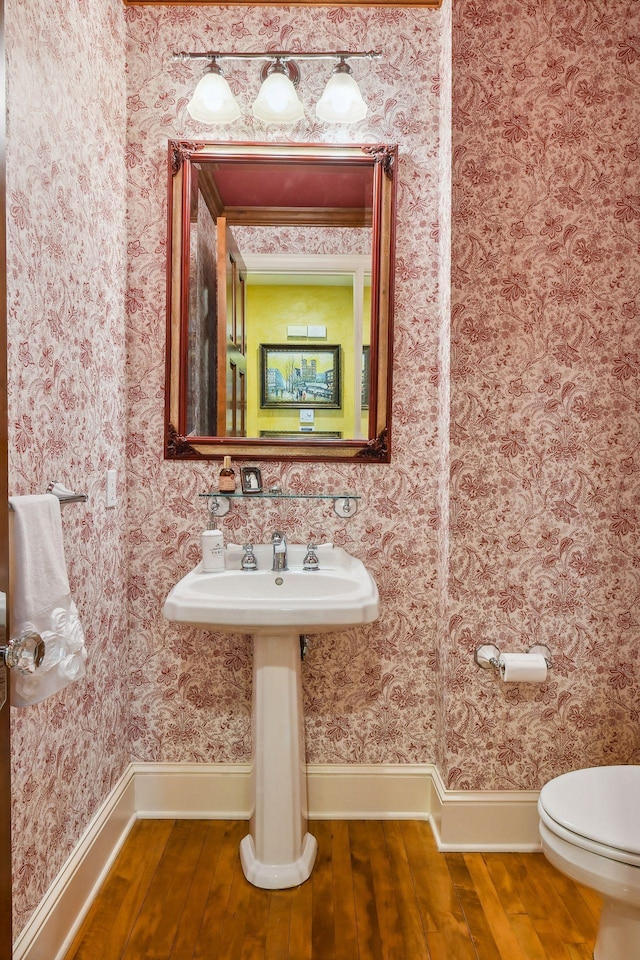 half bath with baseboards, wood-type flooring, toilet, and wallpapered walls