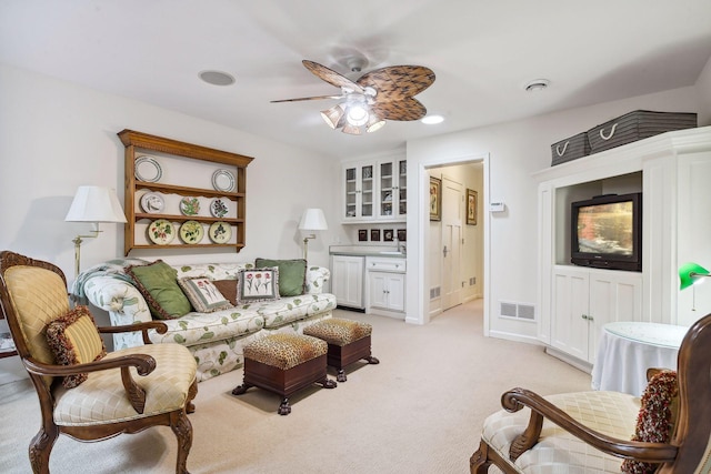 living area featuring visible vents, light colored carpet, baseboards, and a ceiling fan