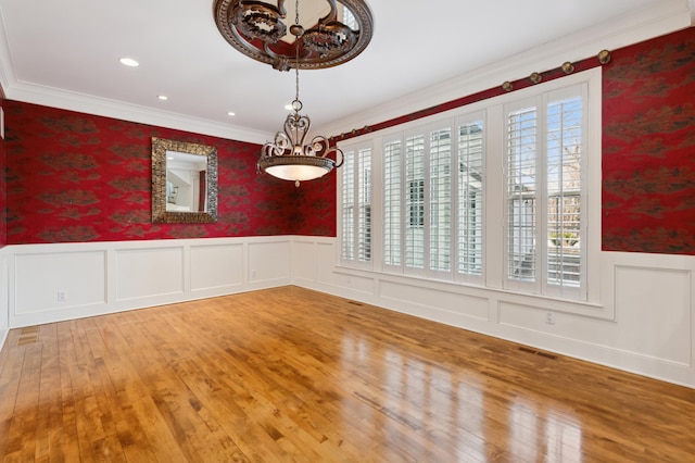 unfurnished dining area featuring a wainscoted wall, visible vents, ornamental molding, hardwood / wood-style flooring, and wallpapered walls