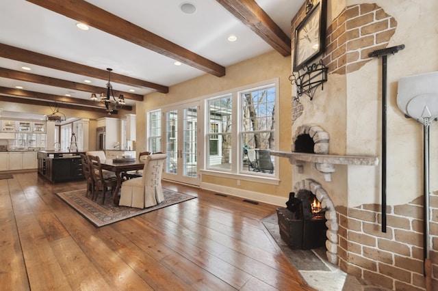 dining area with hardwood / wood-style flooring, beamed ceiling, a fireplace, and visible vents