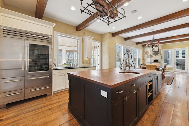 kitchen featuring light wood finished floors, butcher block counters, white cabinetry, and a kitchen island with sink