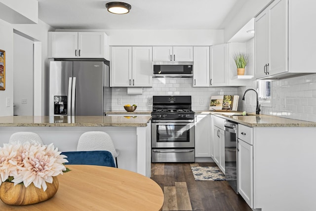 kitchen with appliances with stainless steel finishes, a sink, light stone counters, and white cabinets