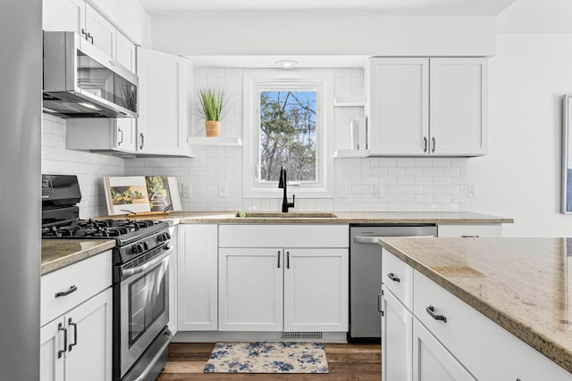 kitchen with dark wood-style flooring, stainless steel appliances, white cabinetry, a sink, and light stone countertops